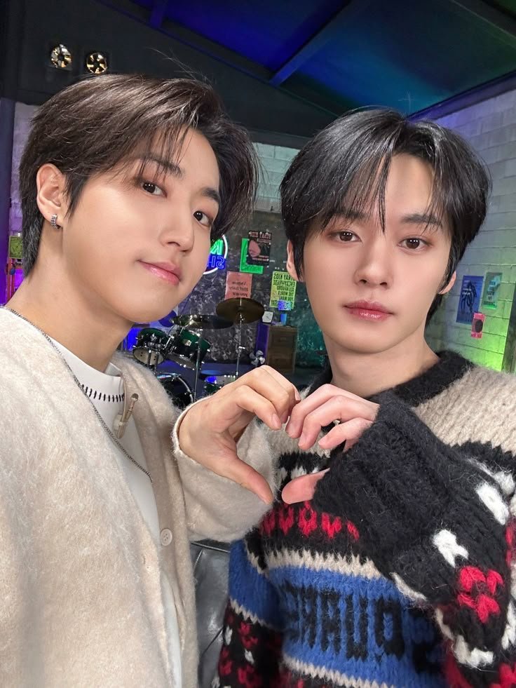 Dos jóvenes, Jisung y Minho de Stray Kids forman un corazón con sus manos en un estudio musical, mostrando afecto y complicidad que los fans suelen shippear