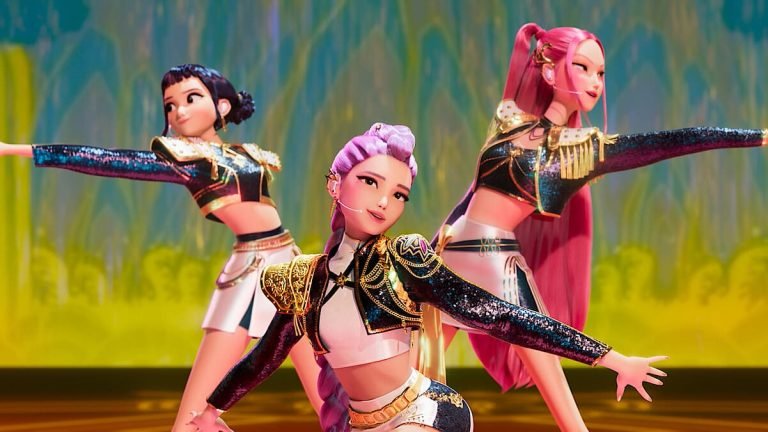 Captura de pantalla del grupo de K-Pop HUNTR/X en un escenario. Las tres protagonistas llevan trajes de actuación de estilo militar y tonos oscuros y dorados, con coreografía sincronizada. KPop Demon Hunters / Netflix